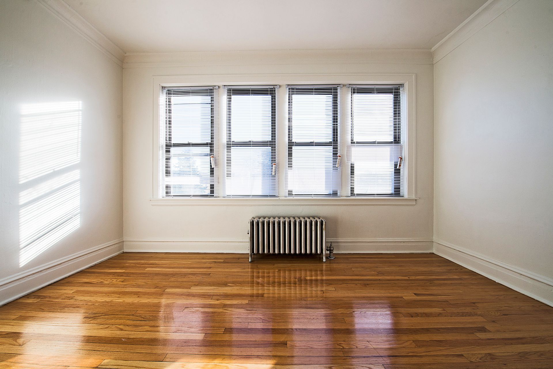 Empty room with wood floor, window with blinds, and radiator.