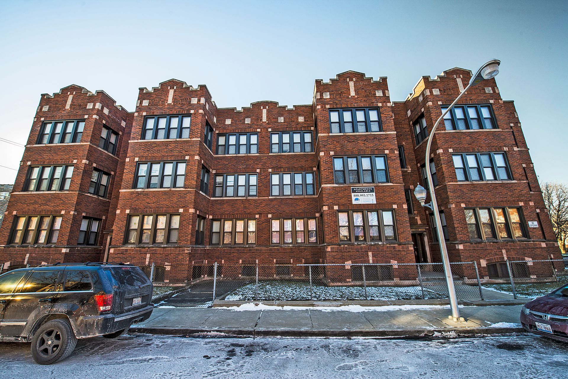 Brick apartment building on a snowy street, with cars parked in front.