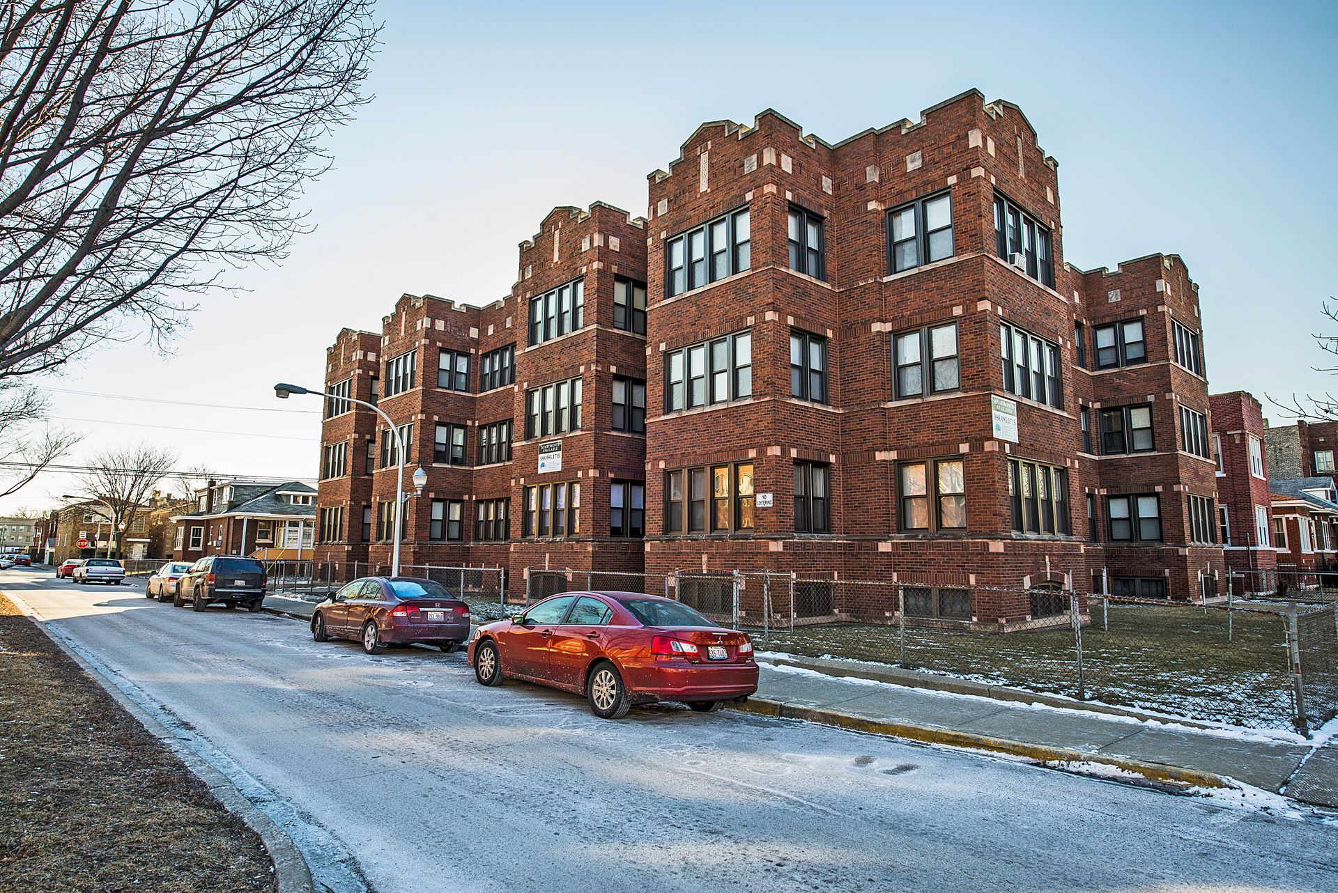 Brick apartment building with parked cars on snow-covered street.