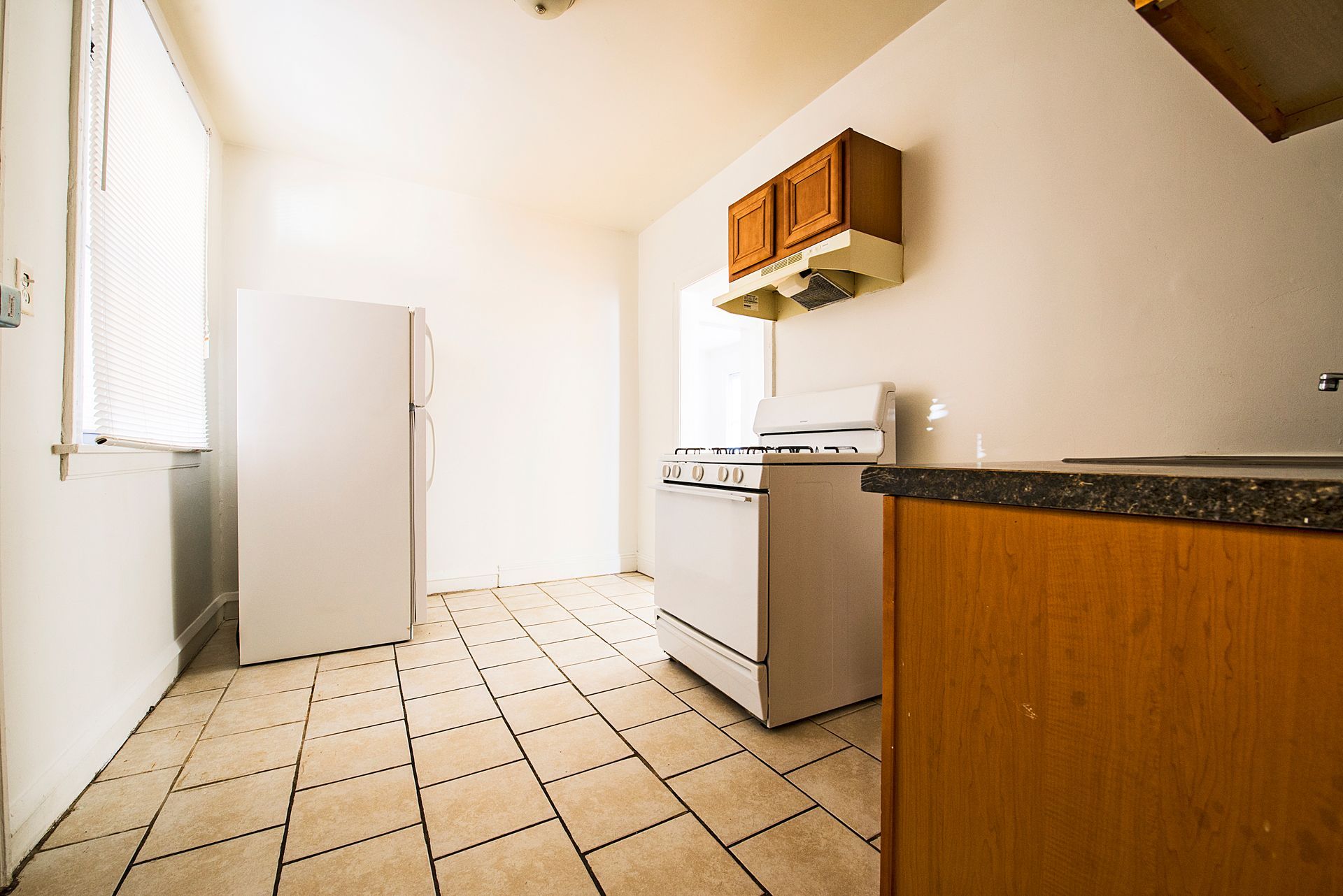 Empty kitchen with white appliances, wooden cabinets, and tile floor.