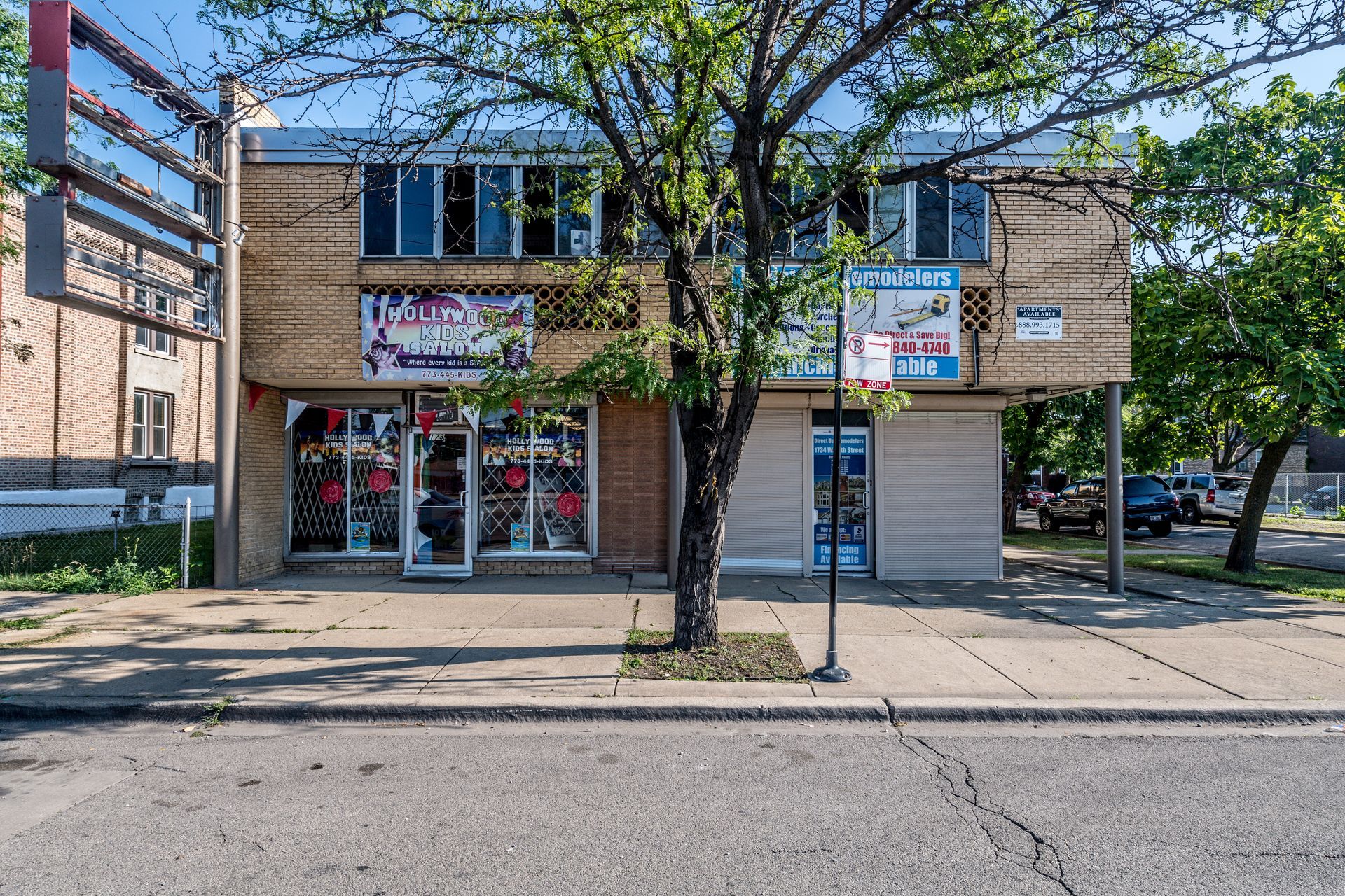 Two-story brick building with storefronts and apartments. A tree stands in front.