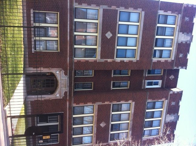 Three-story brick building with multiple windows and decorative details. A wrought iron fence lines the front.
