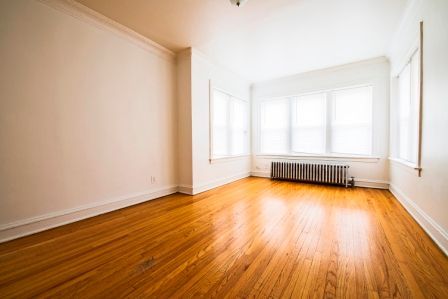 Empty room with wood flooring, white walls, and a radiator beneath a window.