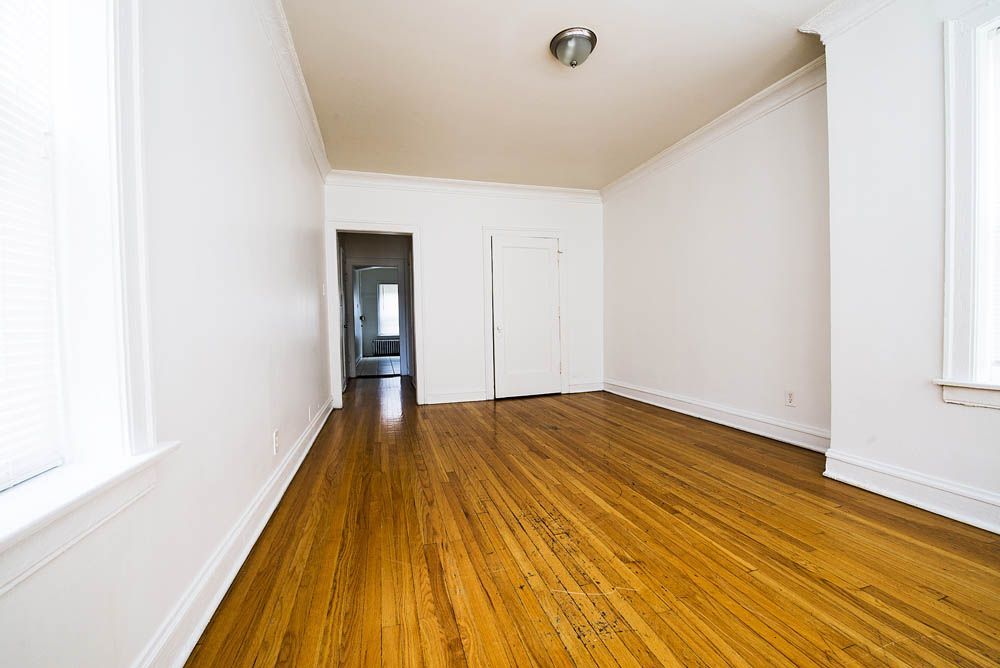 Empty room with hardwood floors, white walls, and a doorway.