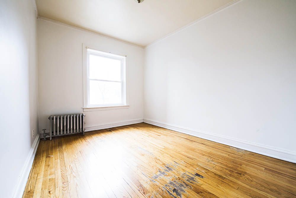 Empty room with hardwood floors, a radiator, and a window.