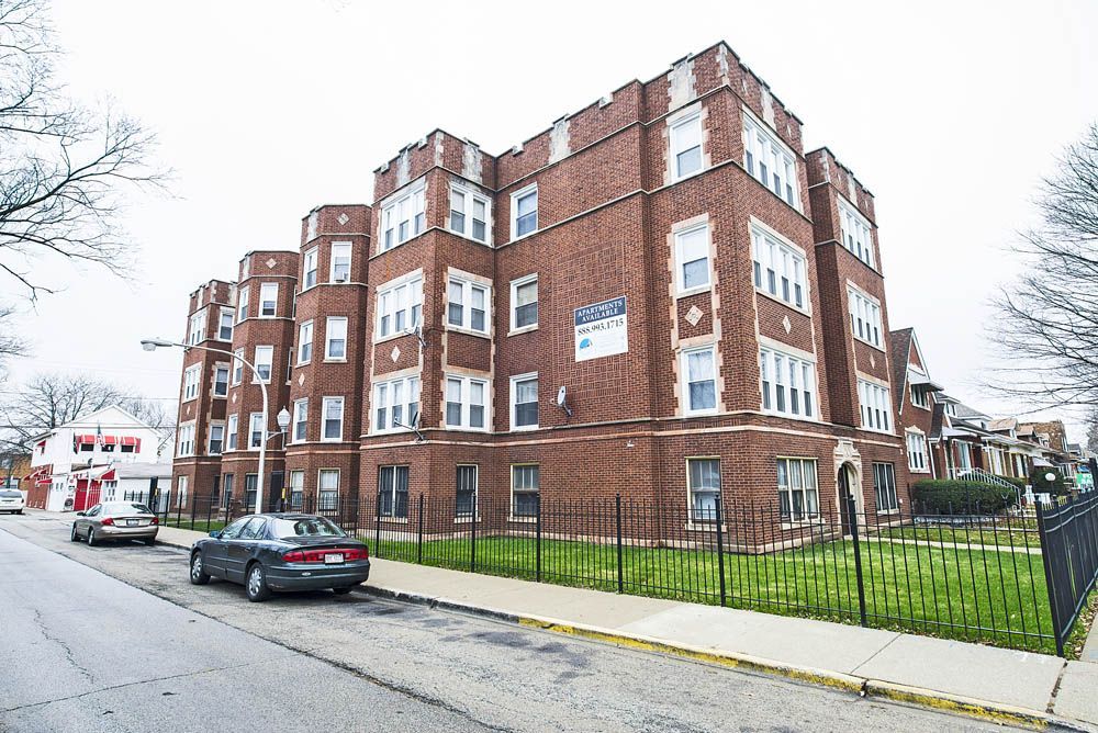 Brick apartment building with decorative details; cars parked on street.