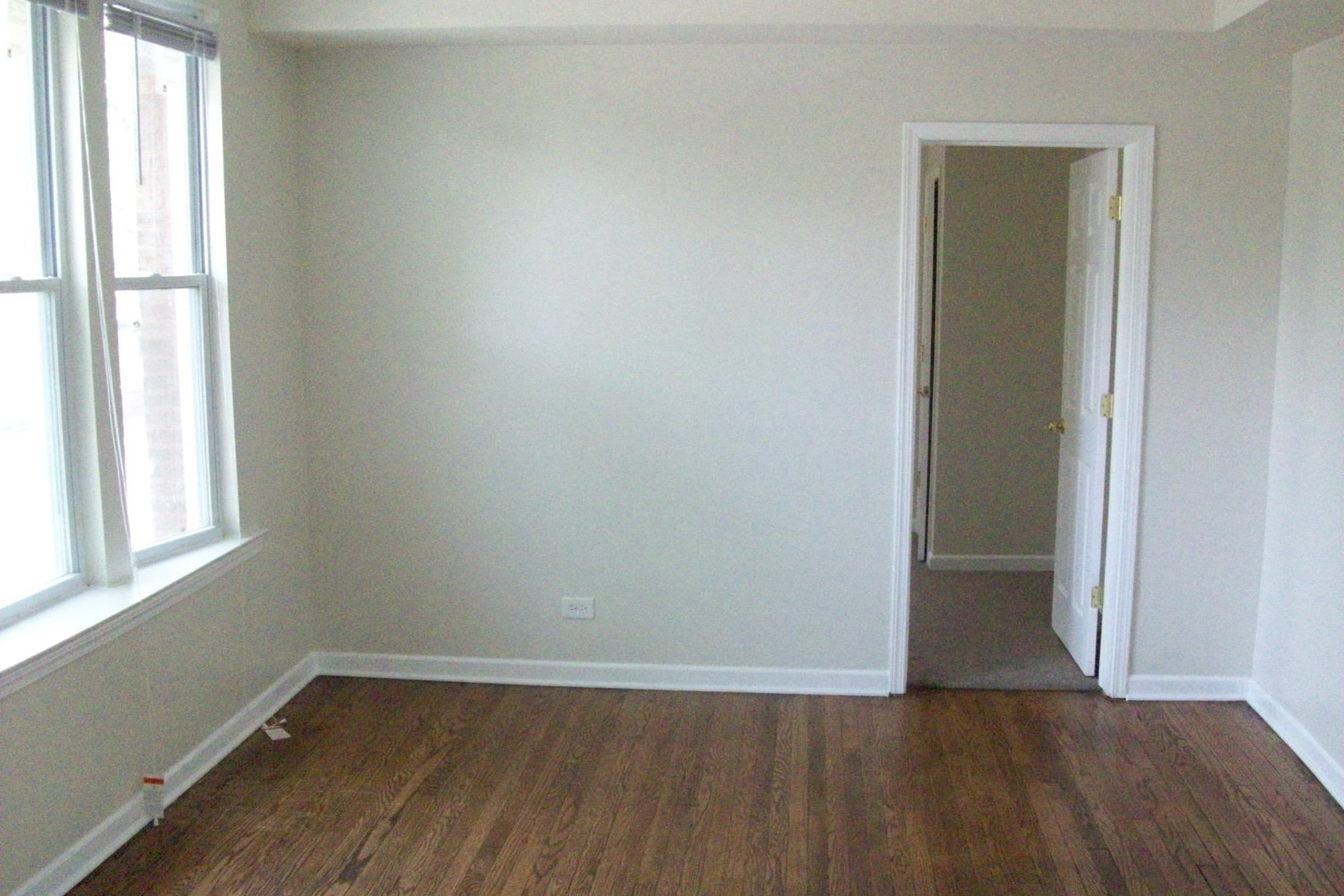 Empty room with hardwood floors, a window, and an open doorway. Walls are light-colored.