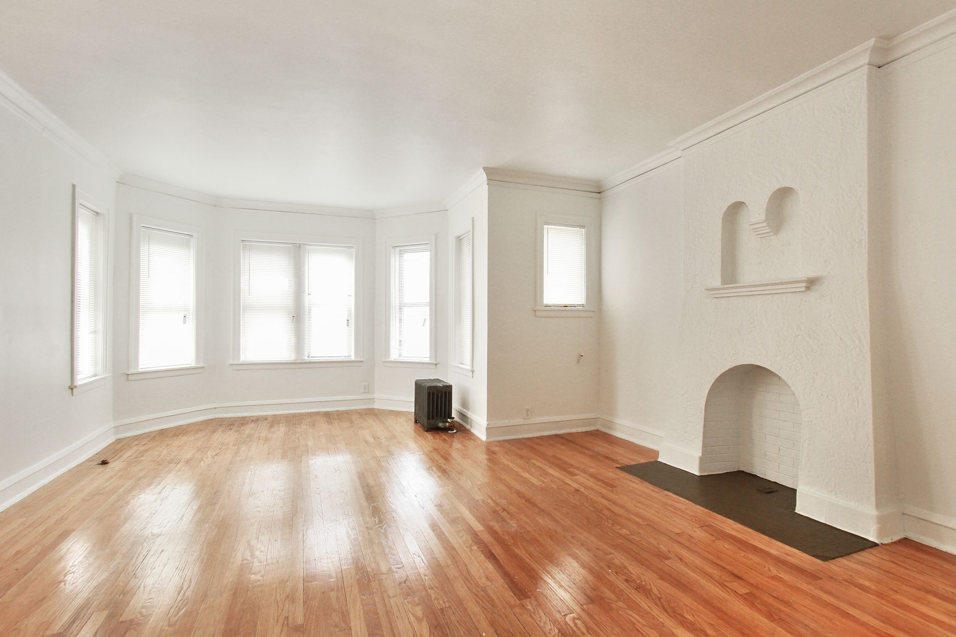 Empty living room with hardwood floors, white walls, and fireplace.