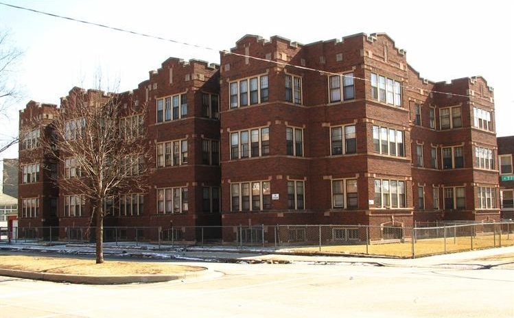 Brick apartment building with multi-pane windows and a fenced perimeter.