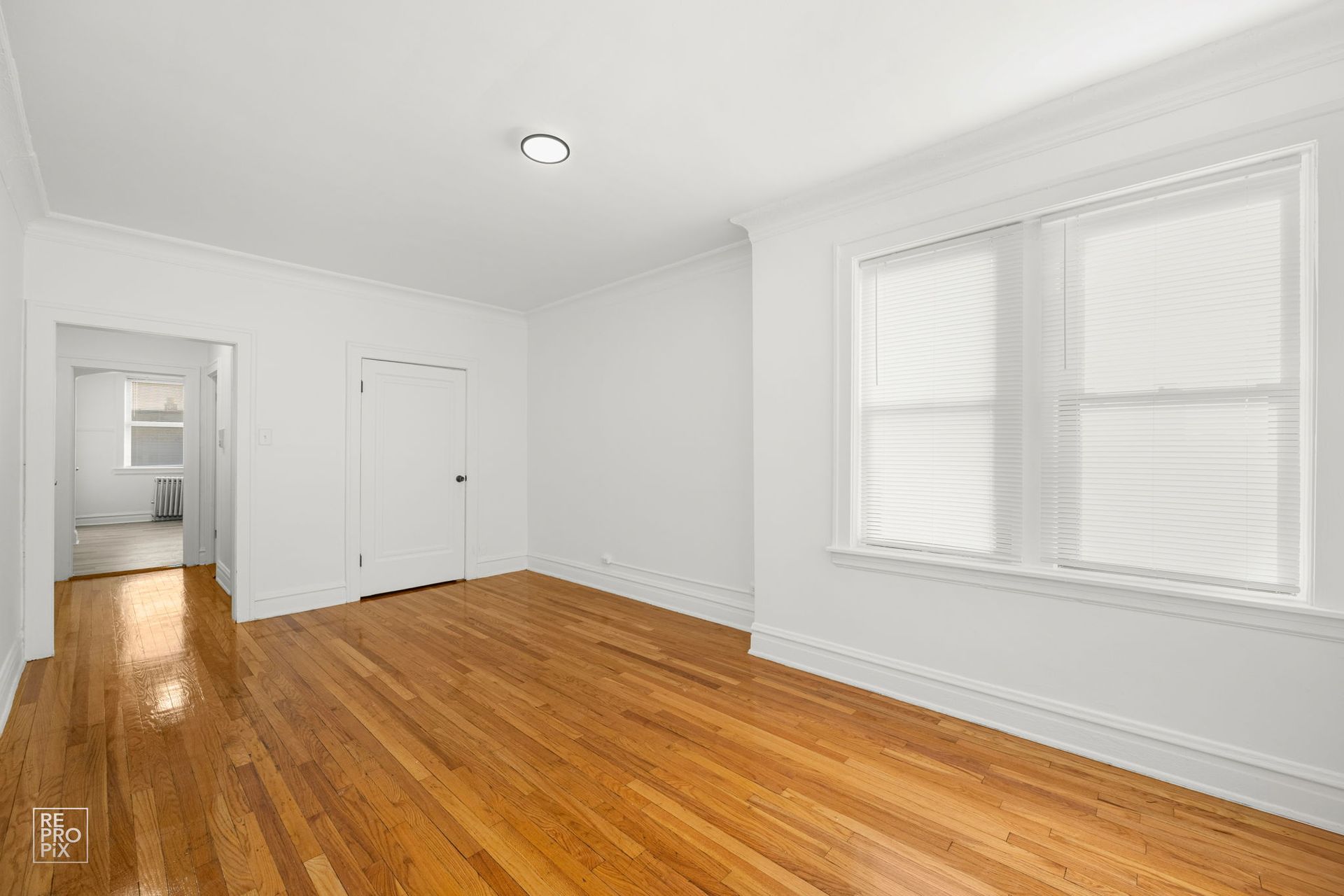 Empty room with hardwood floors, white walls, and a window.