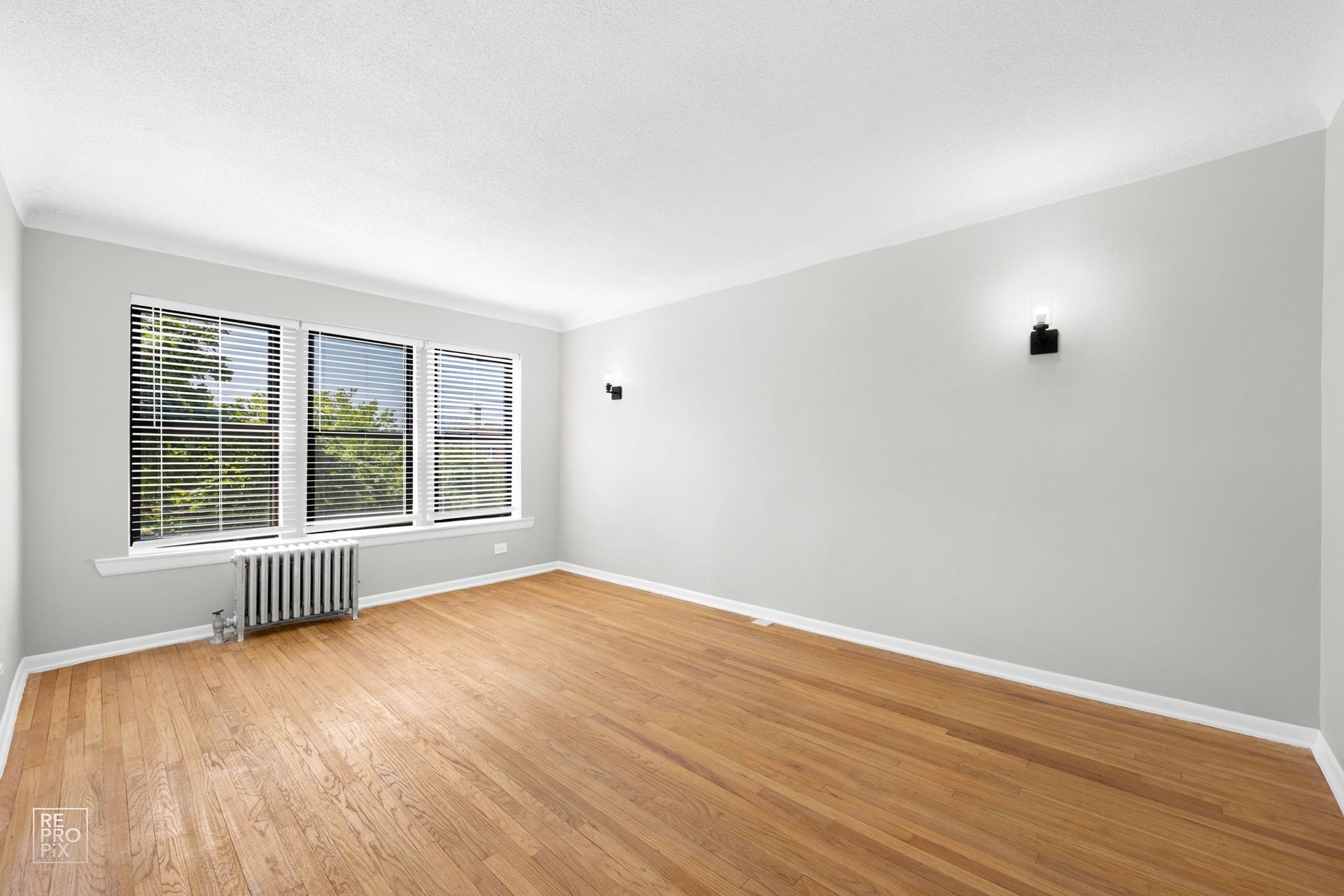 Empty room with hardwood floors, three windows, and two wall sconces.