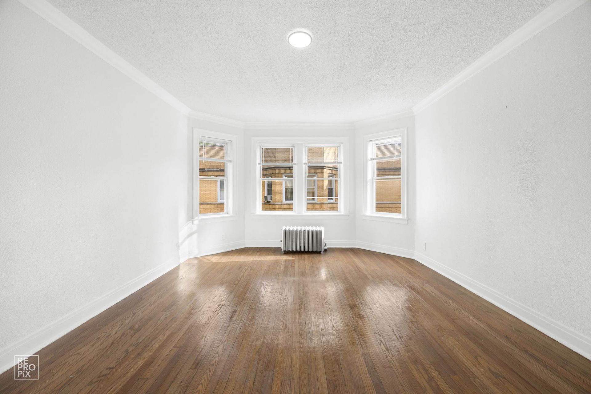 Empty room with hardwood floors, a bay window, and a ceiling light.