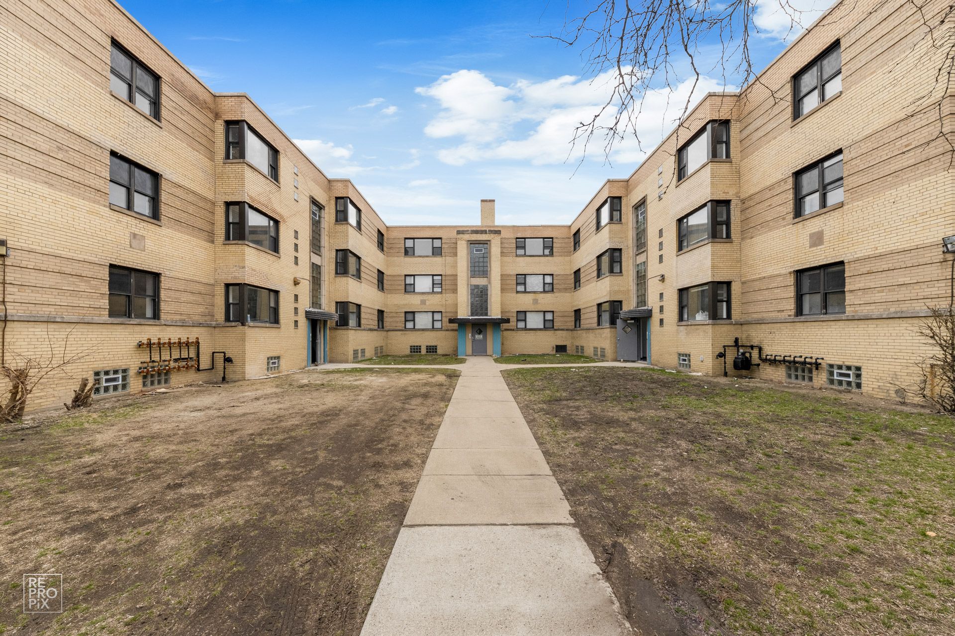 Beige brick apartment building with a central walkway and blue sky.