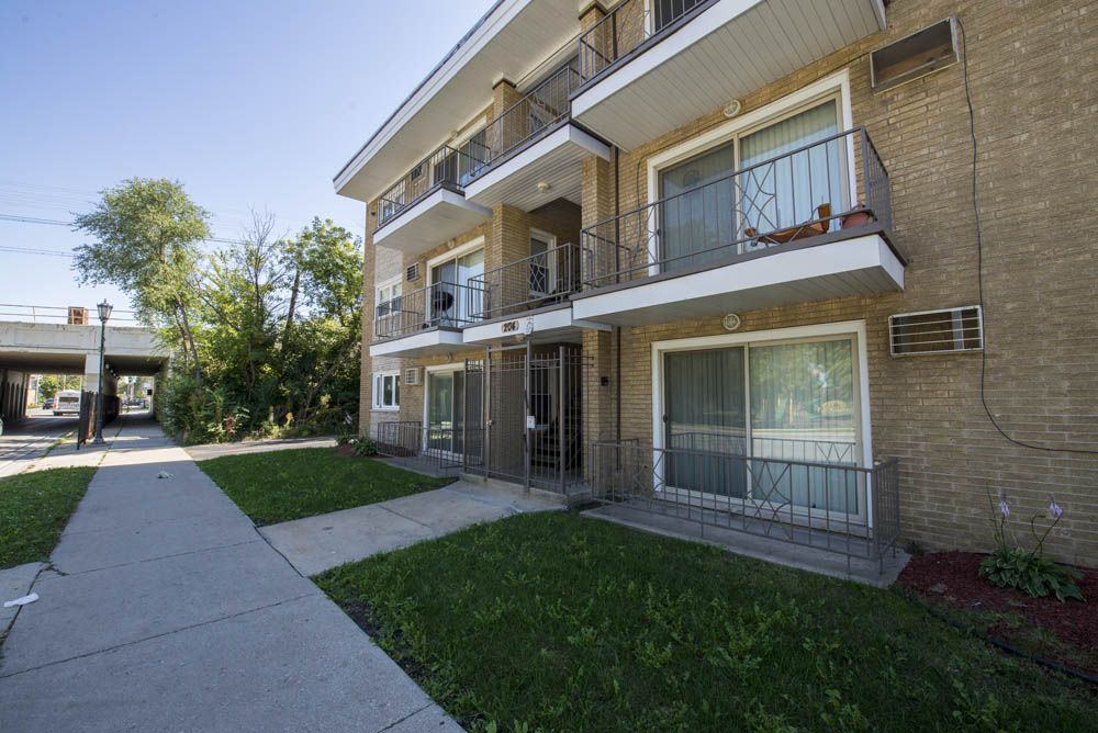 Apartment building exterior with balconies, brick, and grass lawn. Bright day.
