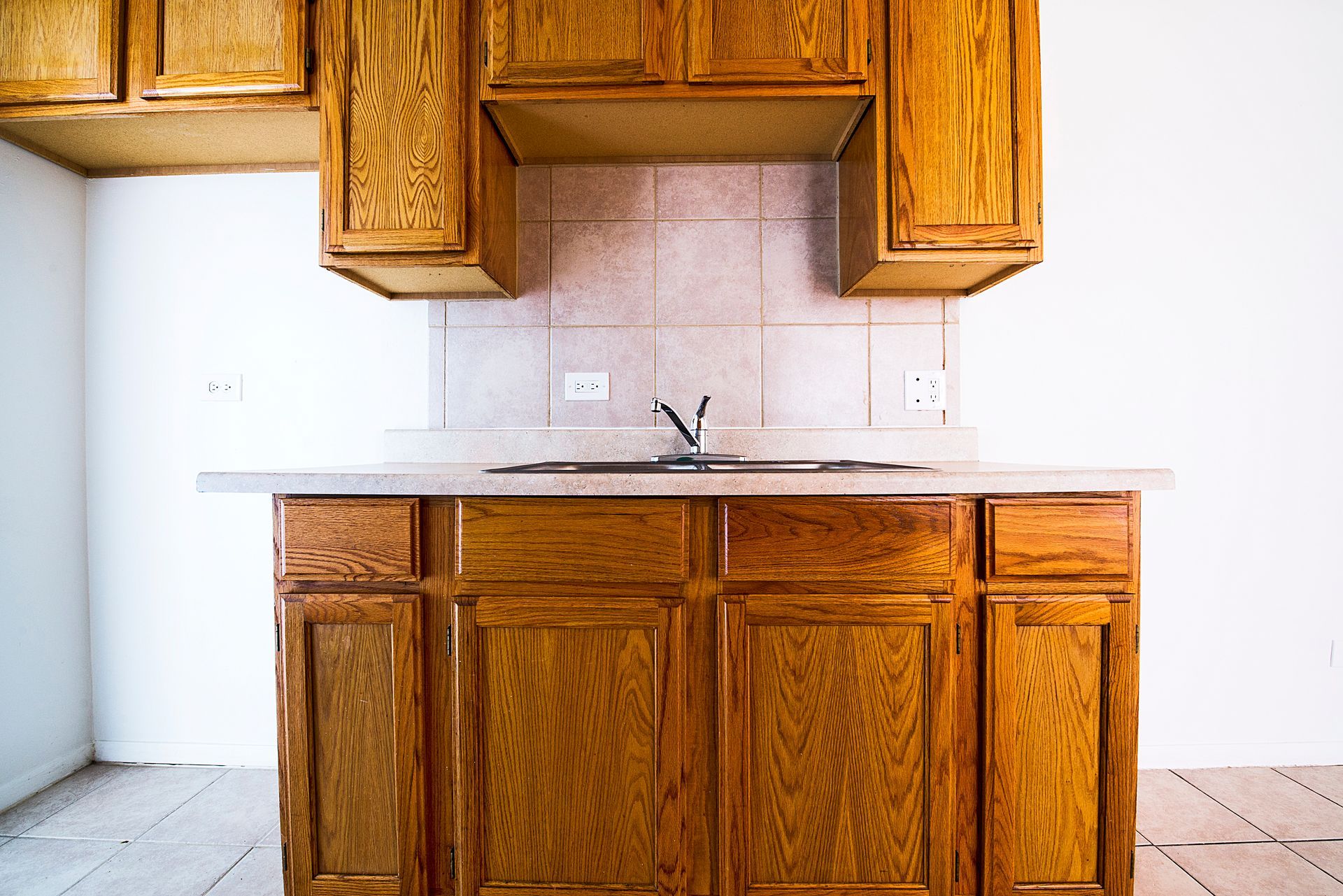 Wooden kitchen cabinets and sink, with beige tile backsplash and white walls.