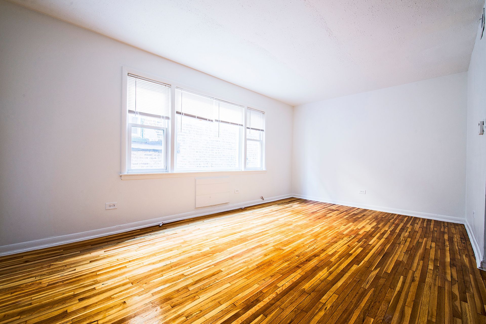 Empty room with hardwood floors, a window, and white walls.