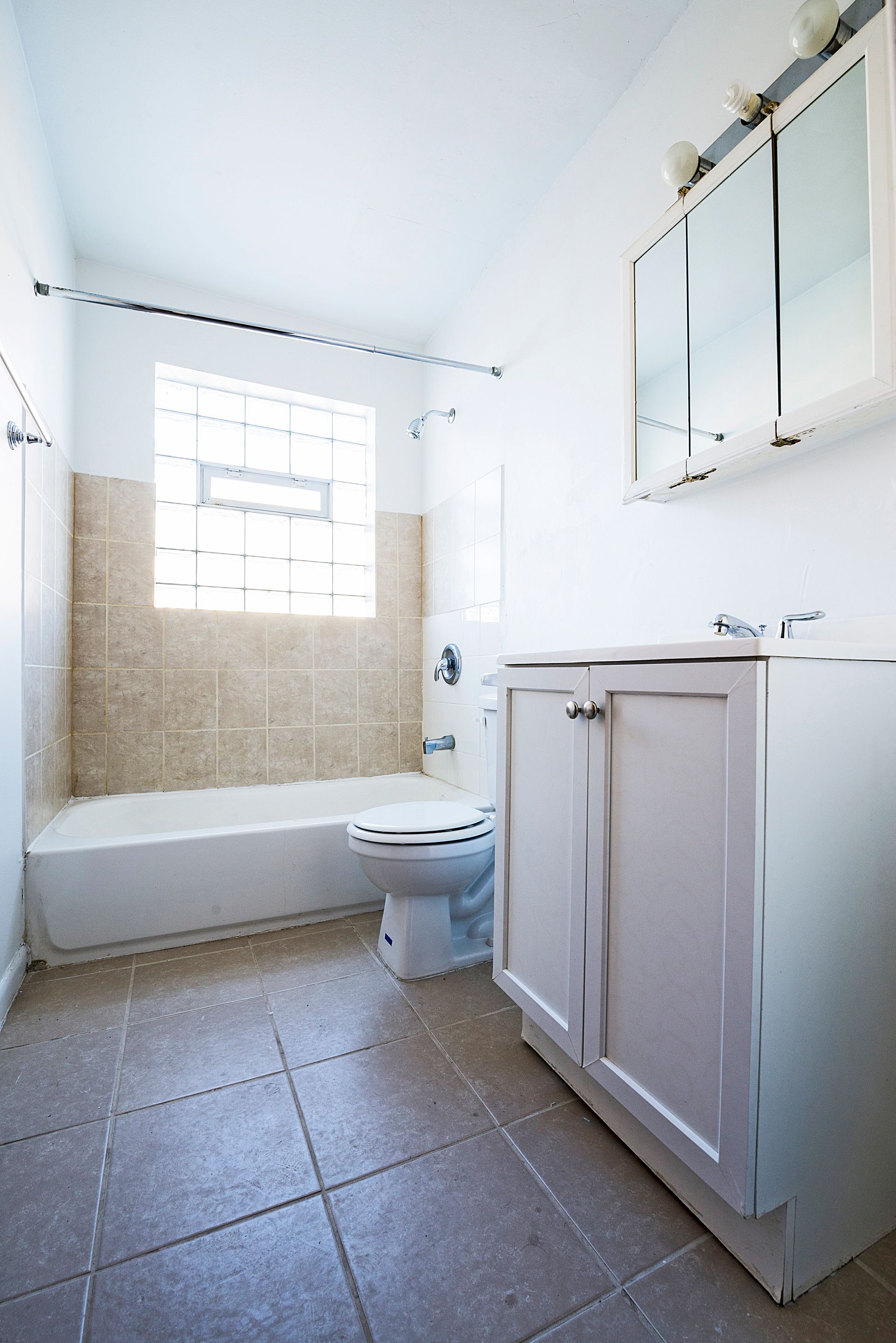 Bathroom with white walls, tan tile, white vanity, and a window with glass blocks.
