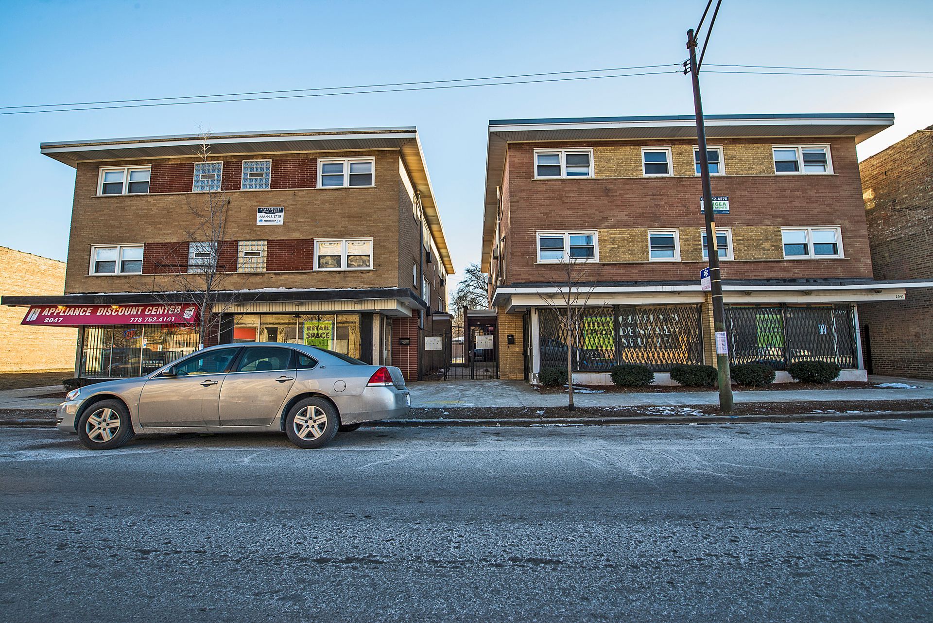 Two-story brick buildings with storefronts and a car parked on a street.