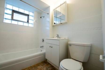 Bathroom with white tiled walls, bathtub, sink, toilet, and a window with glass blocks.