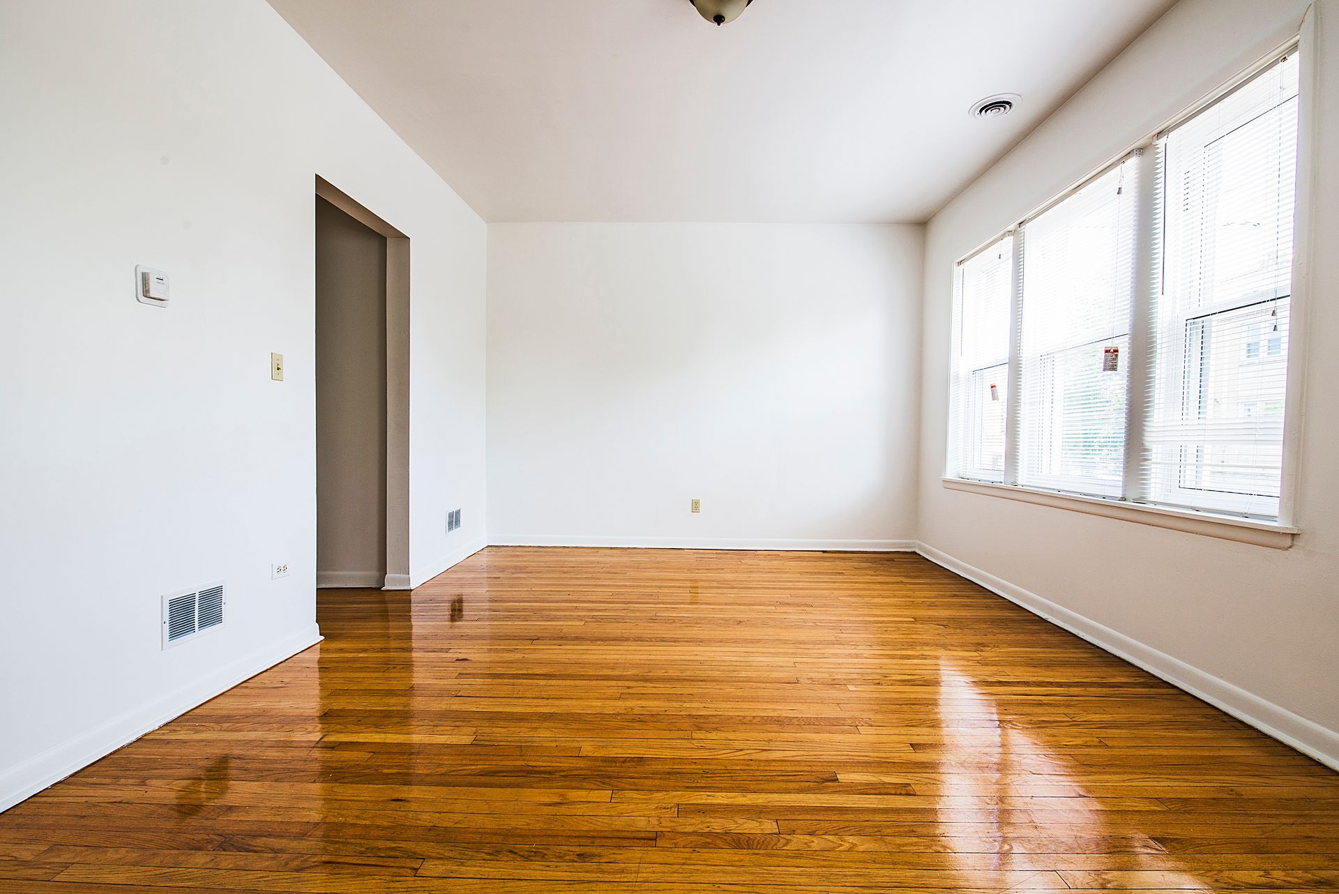 Empty room with hardwood floors, white walls, and a large window.
