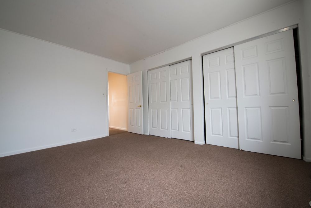 Empty bedroom with brown carpet, white walls and closet doors, and doorway.