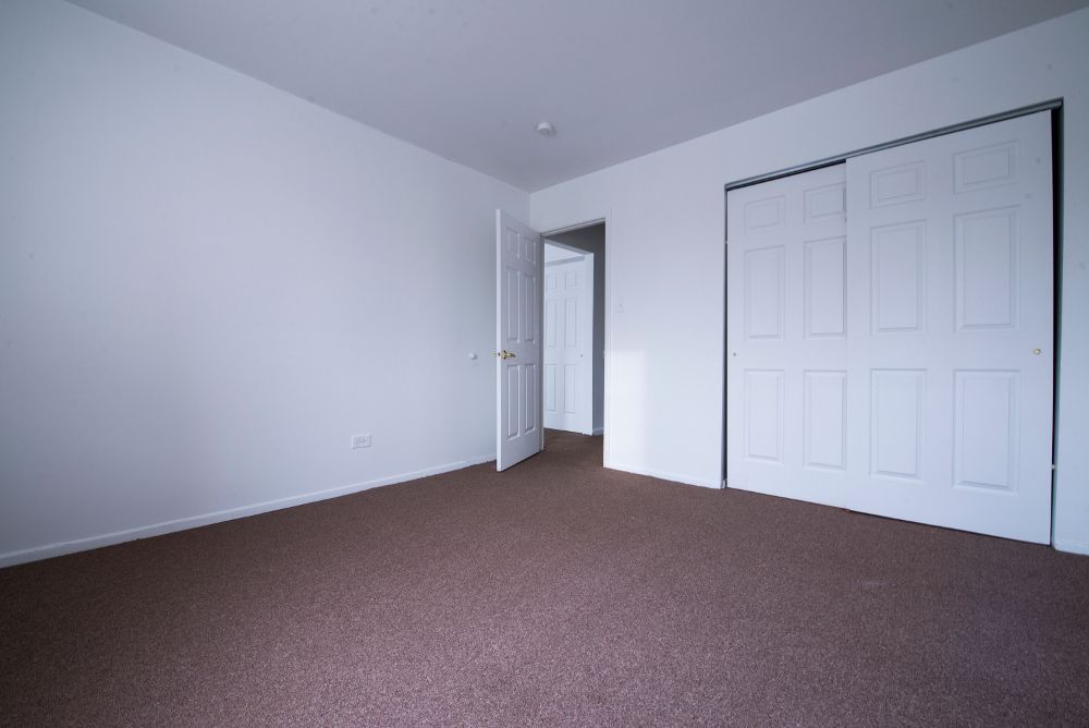 Empty room with brown carpet, white walls, closet doors, and an open doorway.