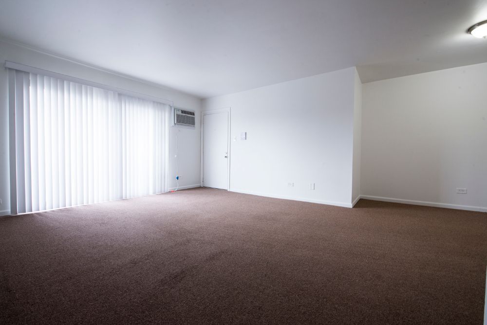 Empty room with brown carpet, white walls, and vertical blinds. A sliding glass door and an air conditioner are visible.
