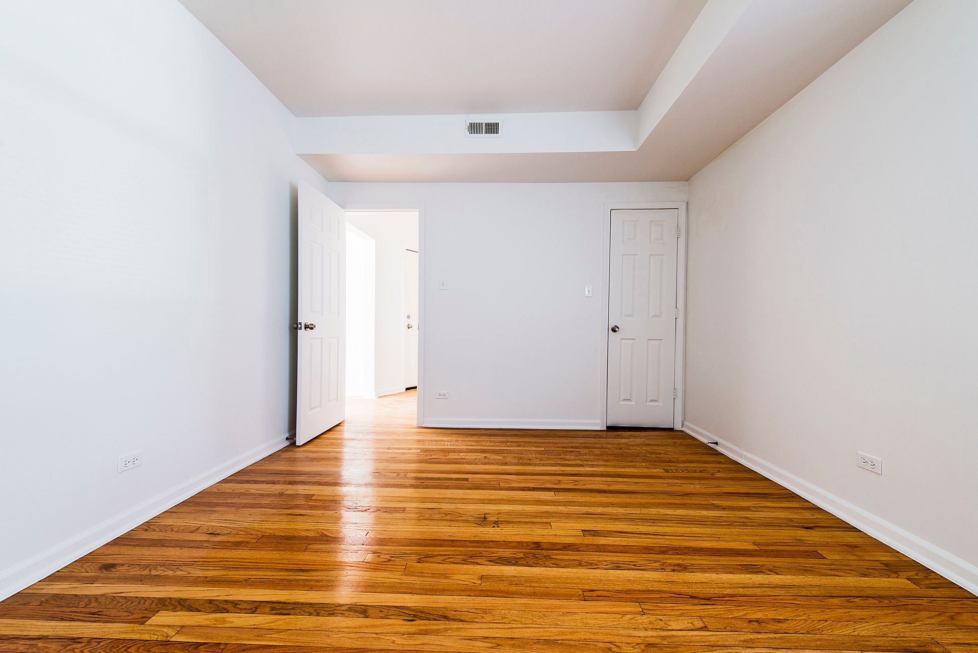 Empty room with hardwood floors, white walls, and two doorways.