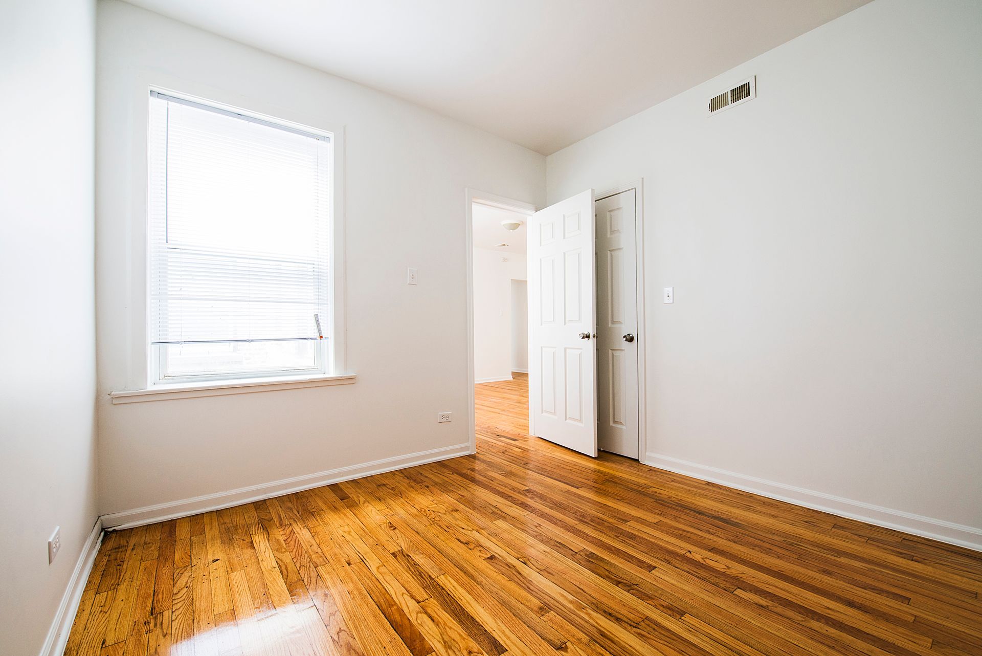Empty room with hardwood floors, white walls, and a window with blinds.