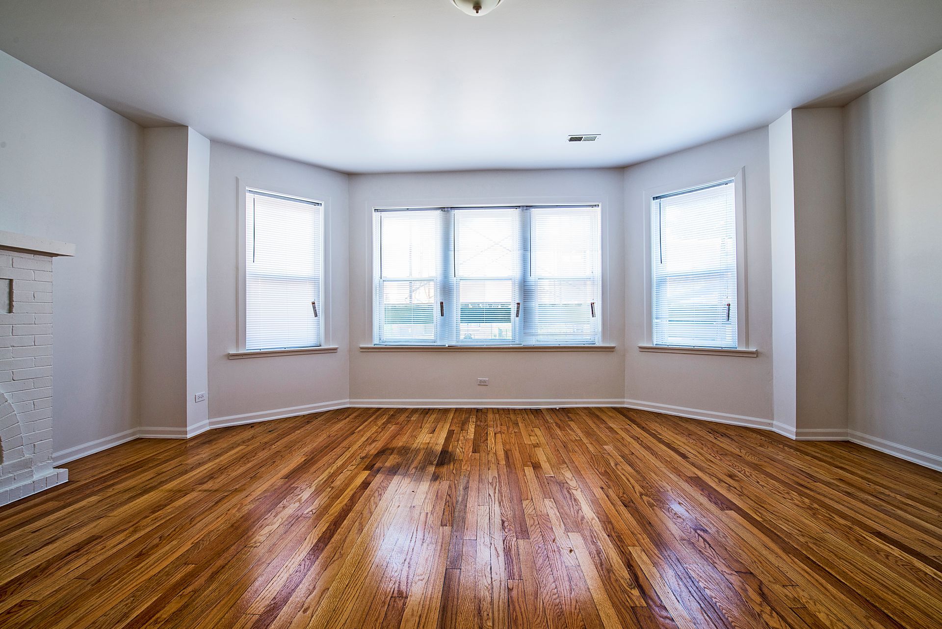 Empty room with wooden floors, bay windows, and white walls.