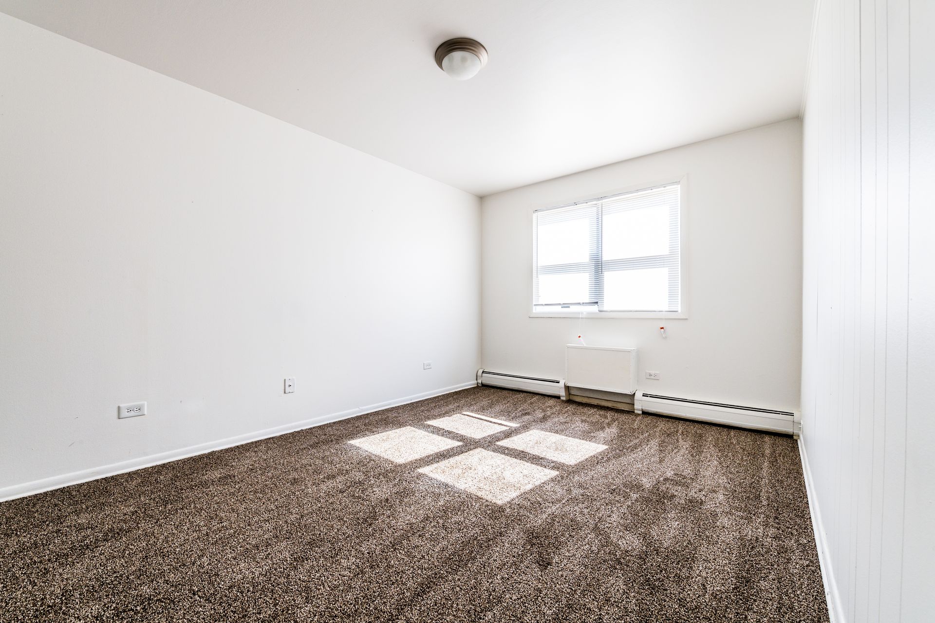 Empty room with brown carpet, white walls, and a window with blinds.