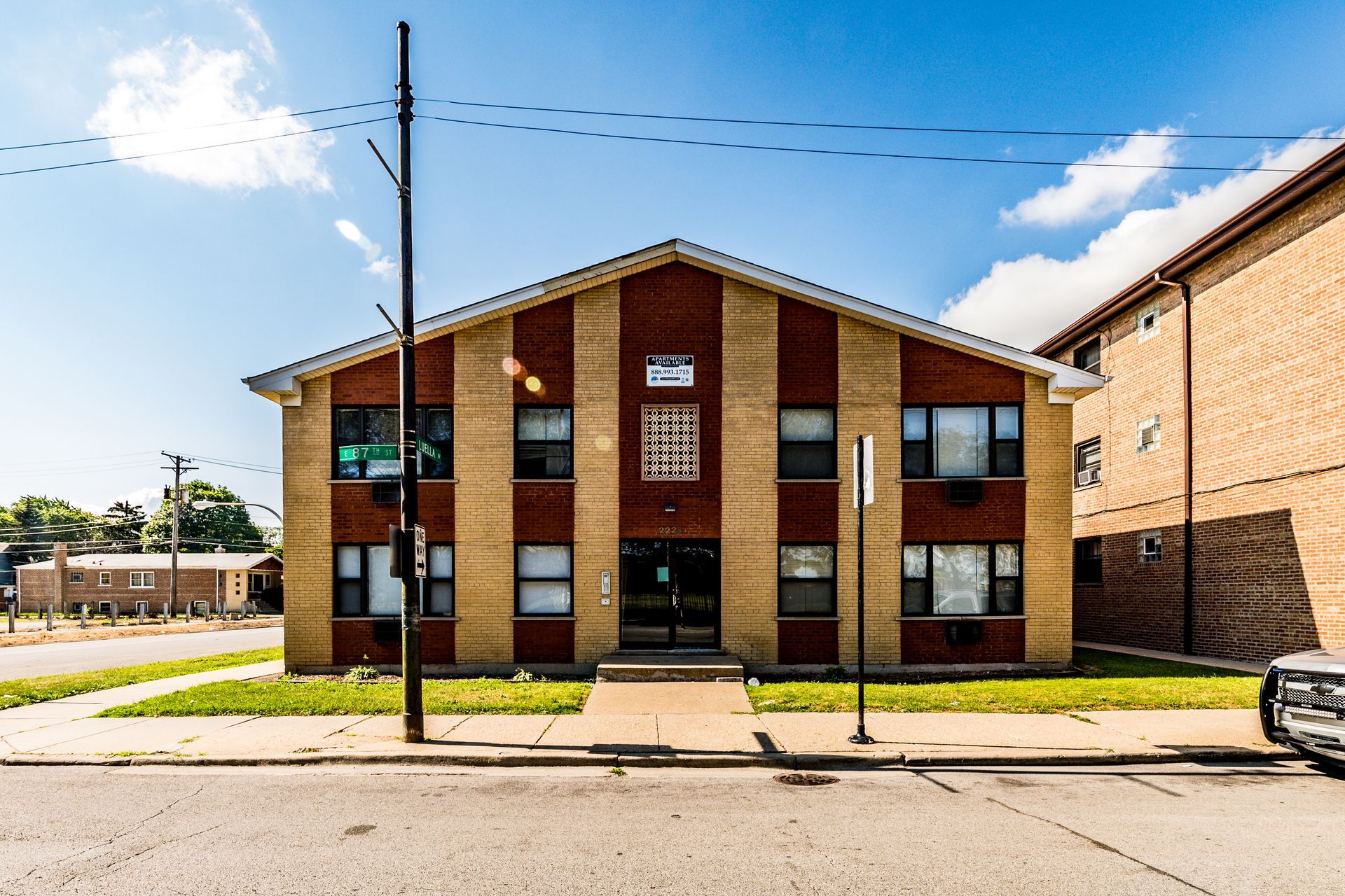 Two-story brick building with tan and brown vertical stripes, front entrance, and street view on a sunny day.