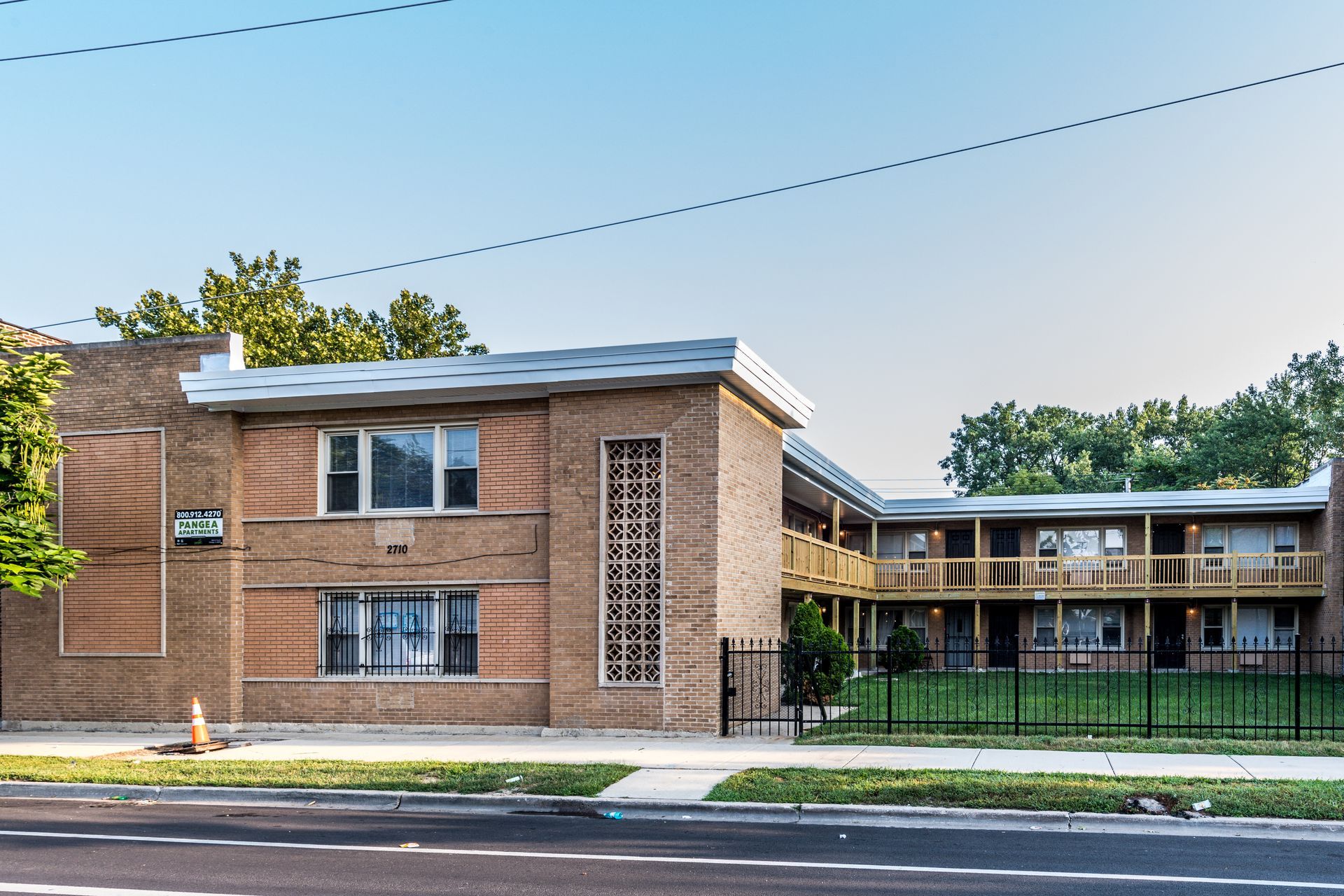 Brick apartment building with balconies, black fence, and trees.