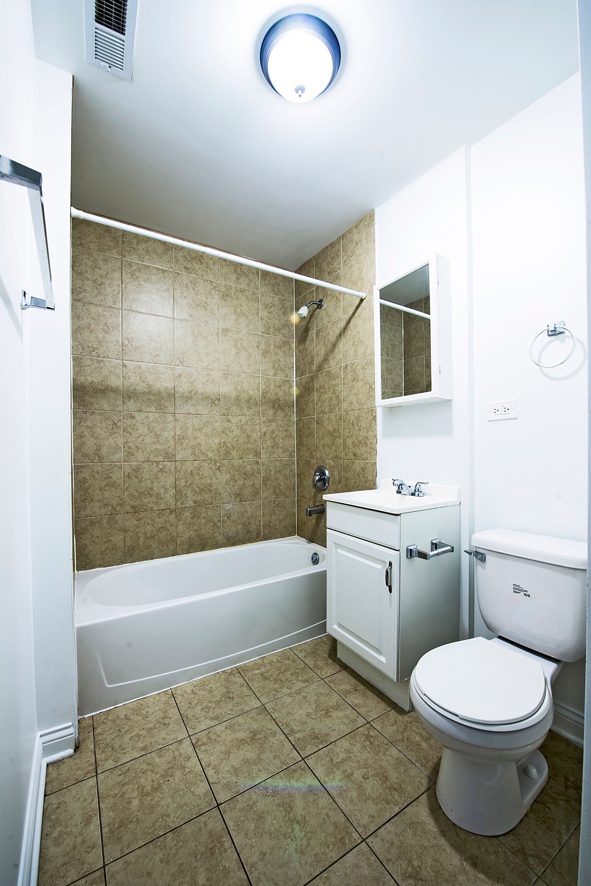 Bathroom with white toilet, vanity, and bathtub. Brown tile in shower area and on floor.