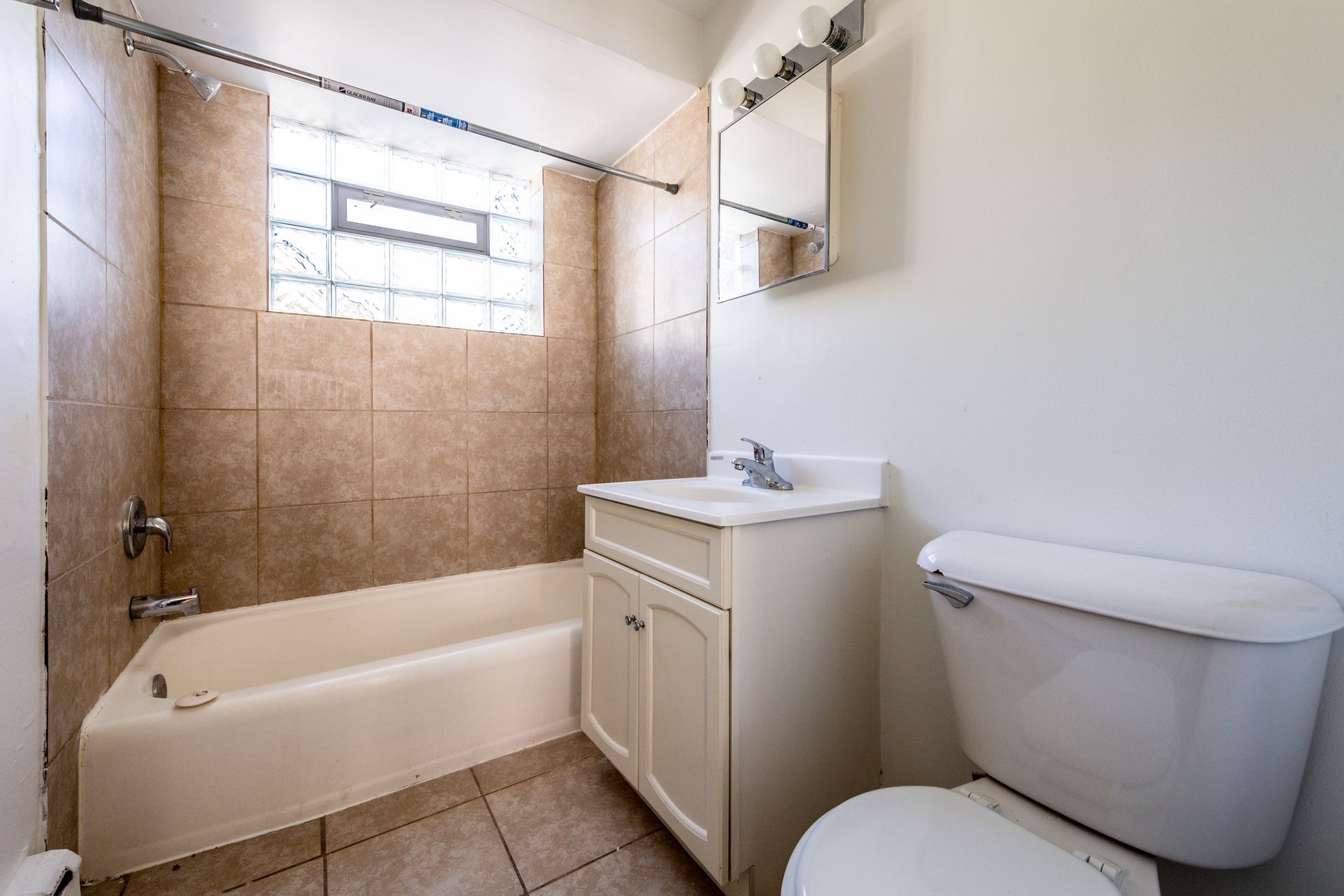 Bathroom with beige tile walls, white fixtures, and a window with glass blocks.