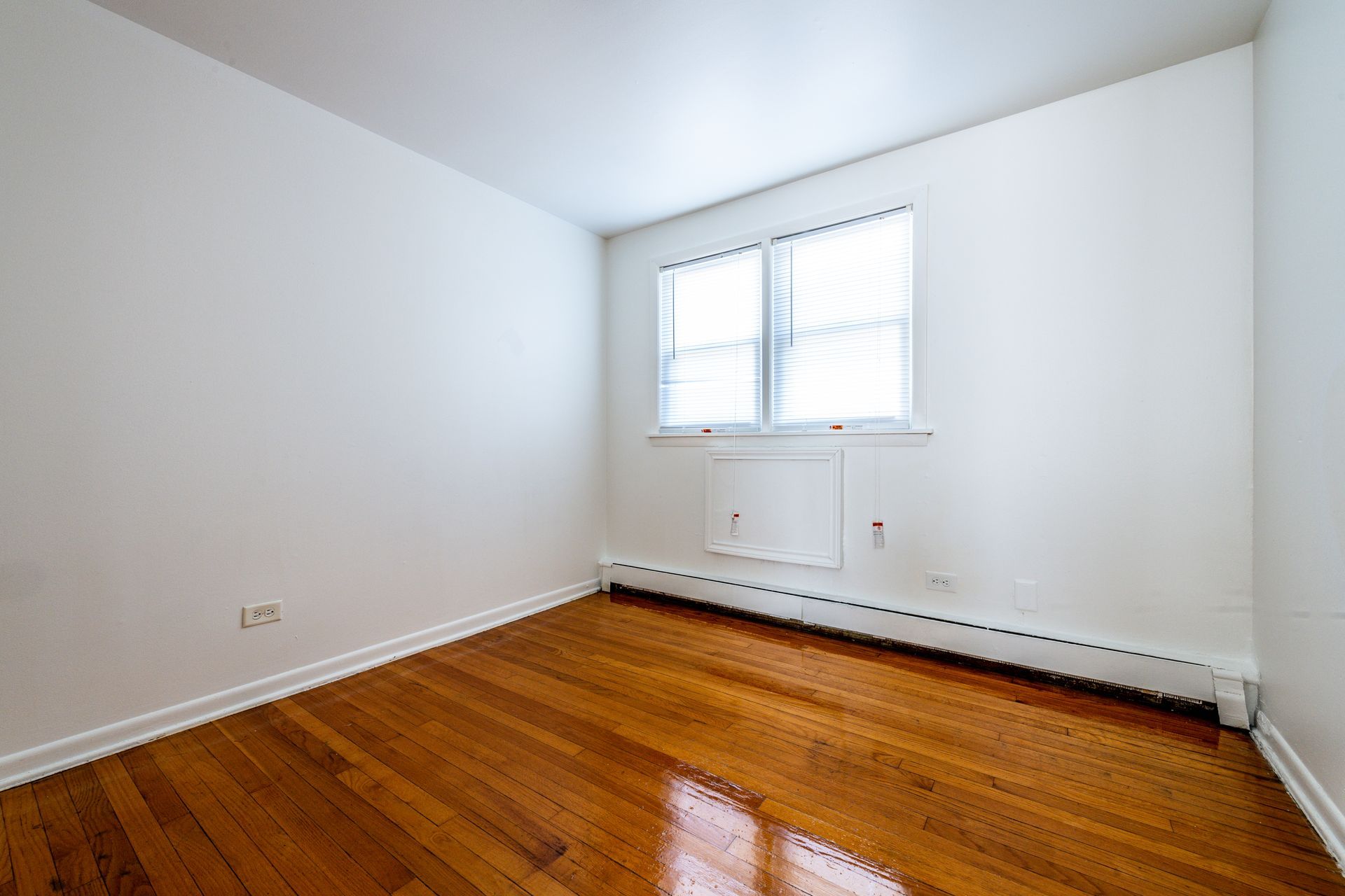 Empty room with hardwood floors, a window, and white walls.