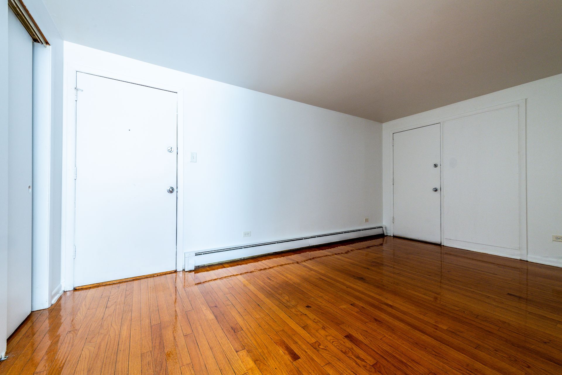 Empty room with wood floors, white walls, two closed doors, and a heater.