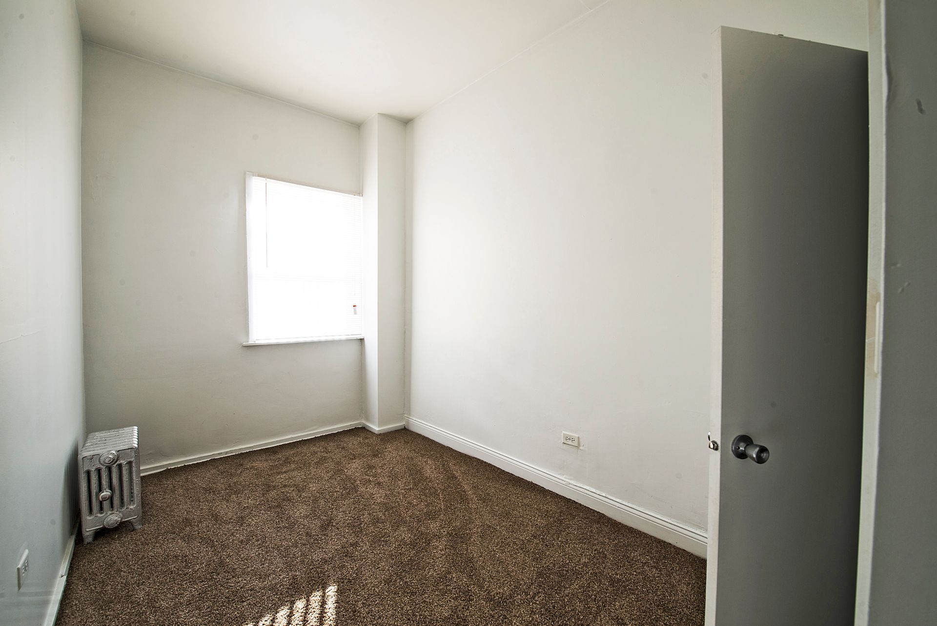 Empty room with brown carpet, white walls, two doors, and natural light.