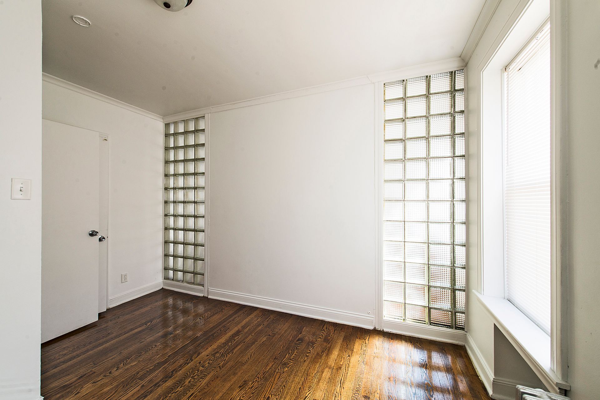 Empty room with glass block windows, a closed door, and hardwood floors.
