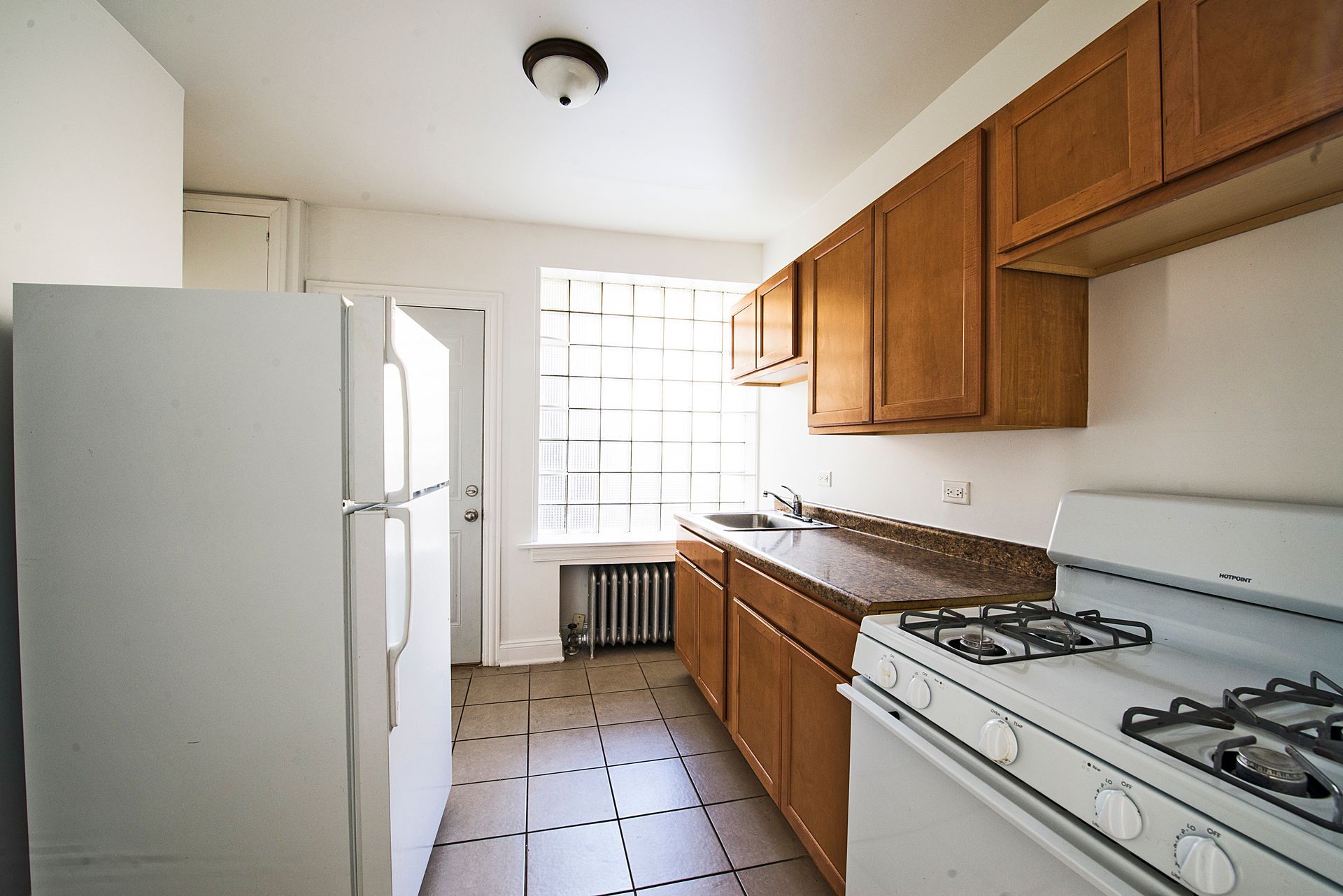 Kitchen with white appliances, brown cabinets, tile floor, and a window.
