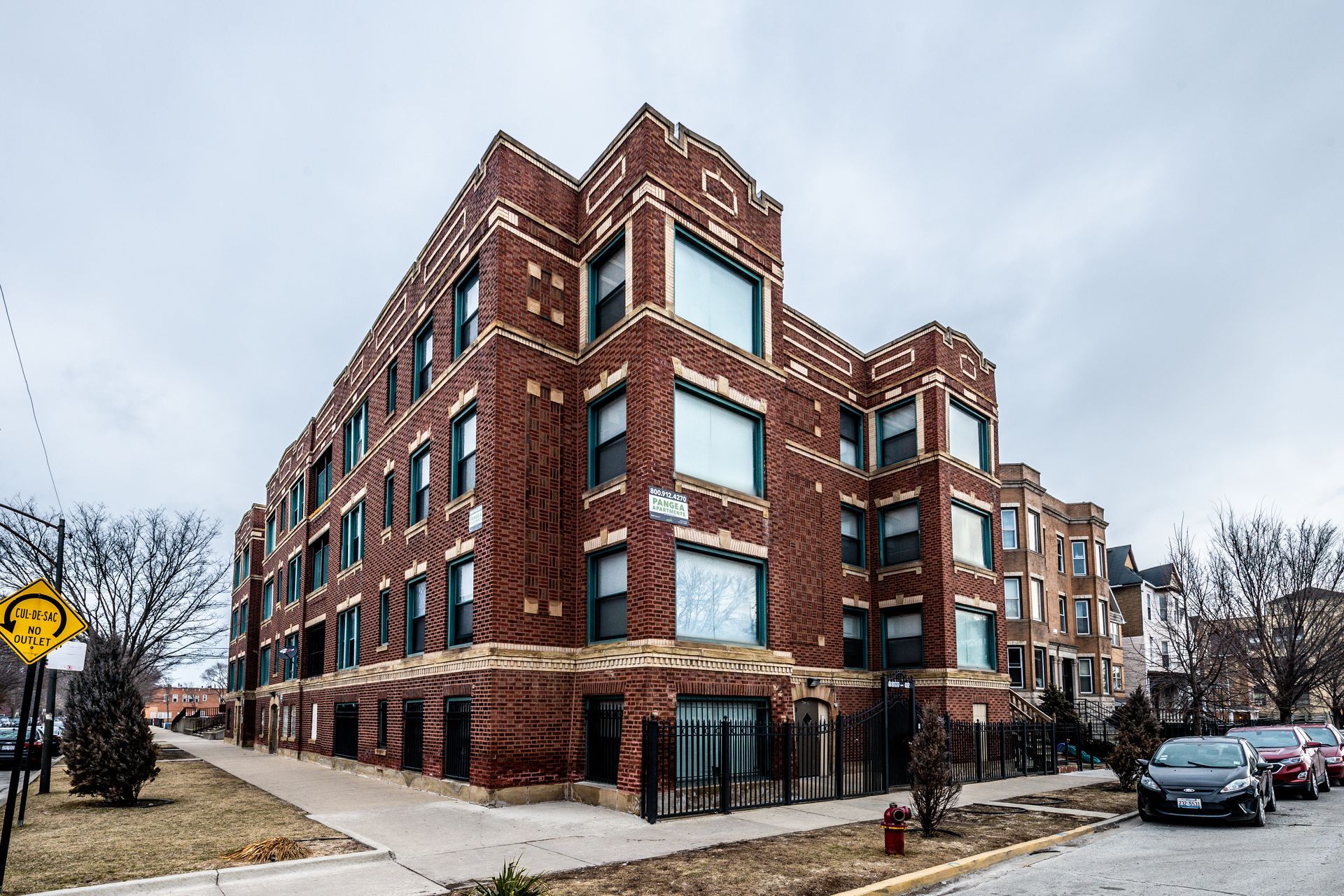 Brick apartment building with large windows and a cloudy sky.