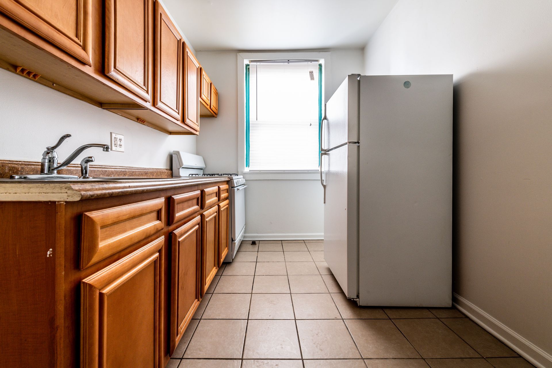 Kitchen with wooden cabinets, a white refrigerator, and a window with blinds.
