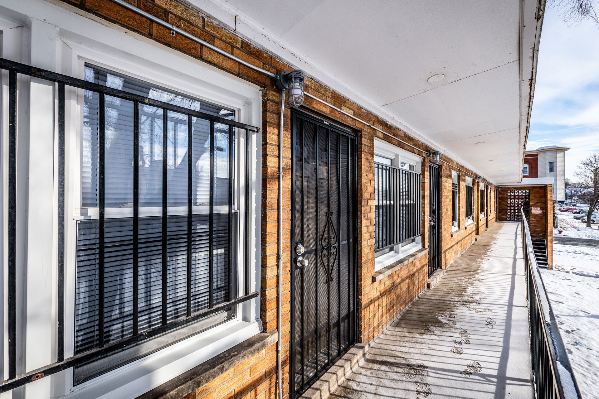 Exterior view of a brick building hallway with windows, black metal door, and snow.