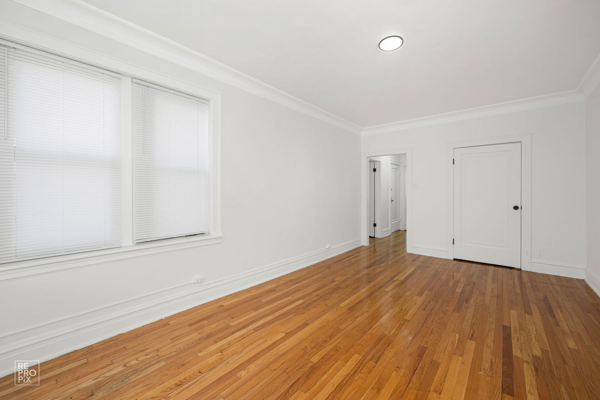 Empty room with hardwood floors, white walls, and a window with blinds.