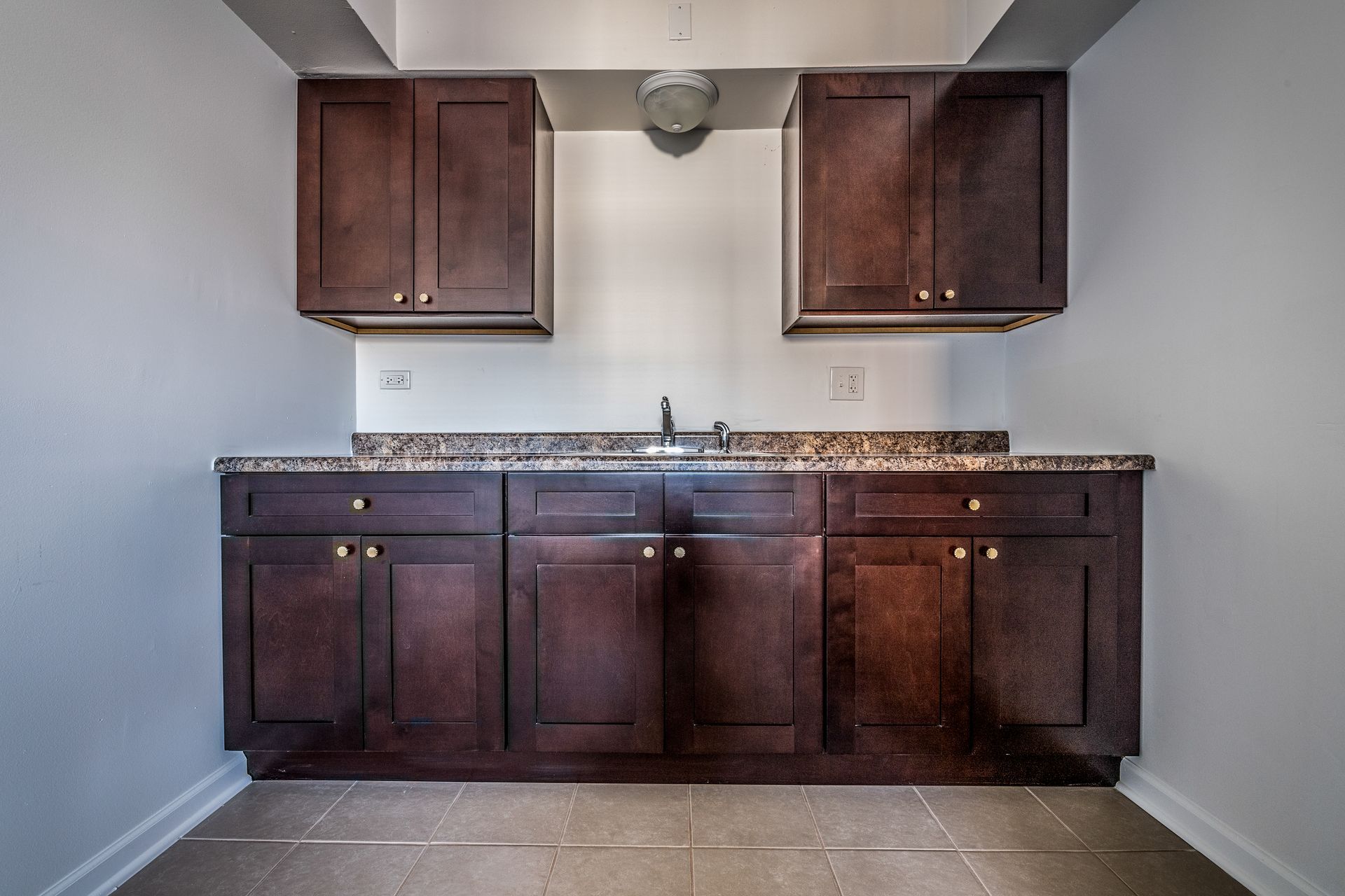Dark wood cabinets with a granite countertop and a sink in an empty room.