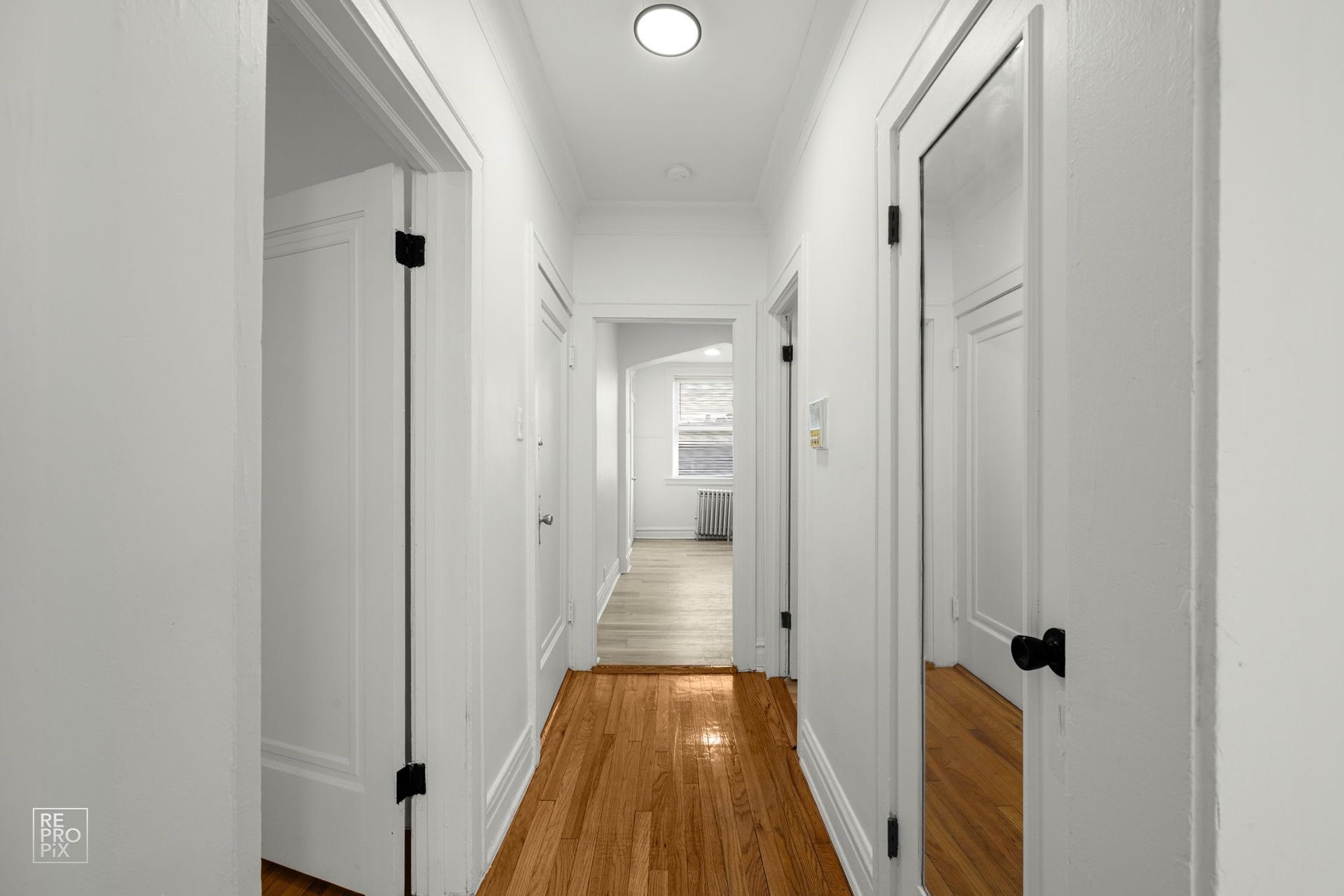 Hallway with white walls, wooden floor, and black door hardware. Doors line the sides, leading to other rooms.
