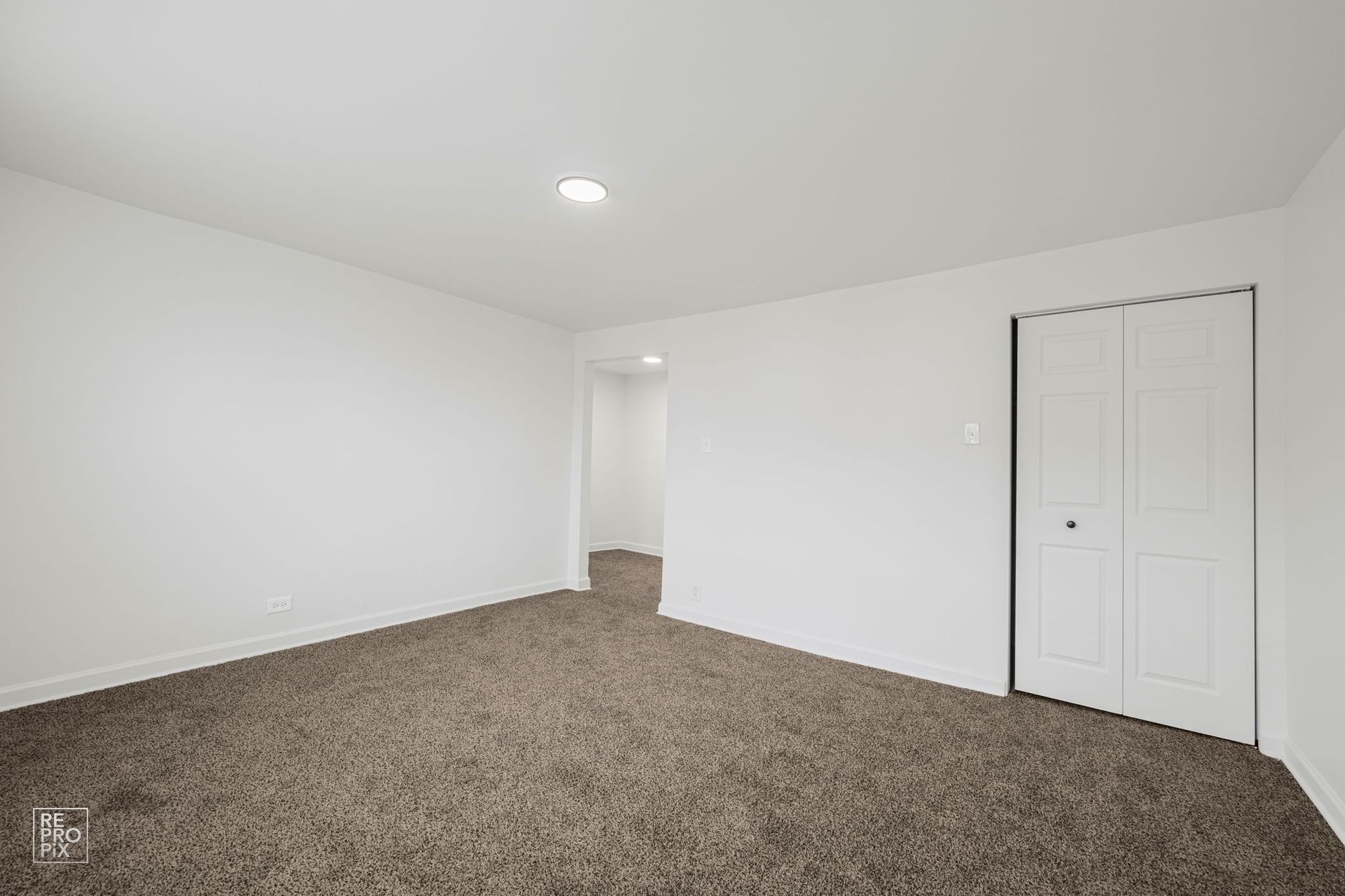 Empty room with white walls, brown carpet, and a closed white closet door.