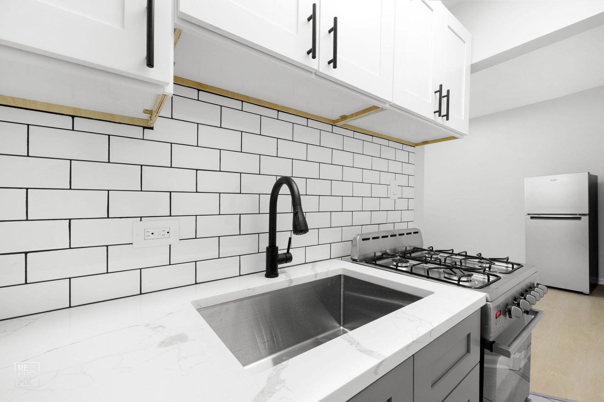 Kitchen with white subway tile backsplash, stainless steel sink and appliances. White cabinets with black hardware.