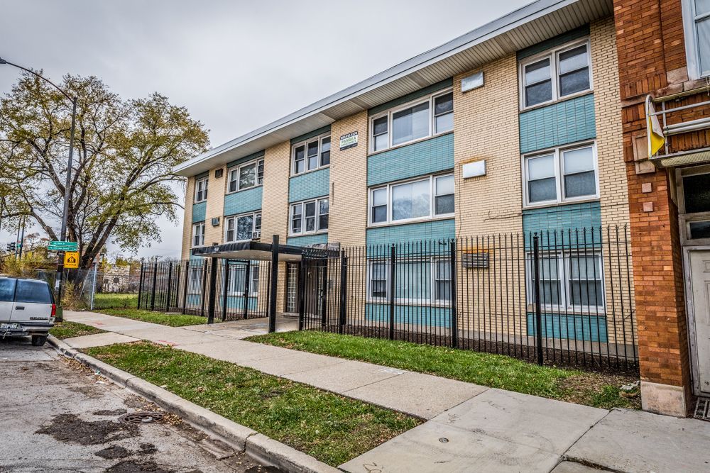 Multi-story apartment building with turquoise accents, black iron fence, and sidewalk.