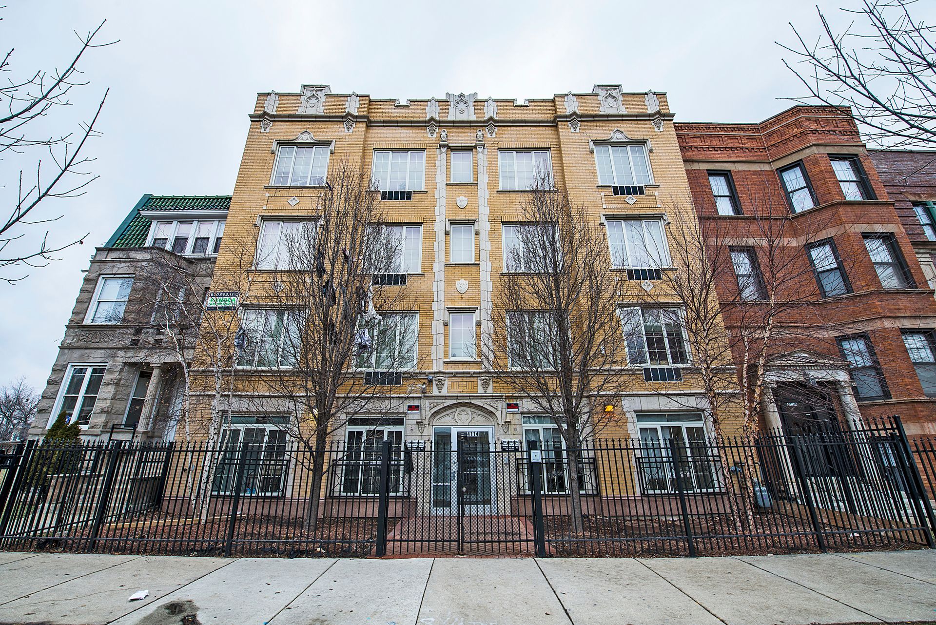 Multi-story apartment building with tan facade, black gate, and bare trees.